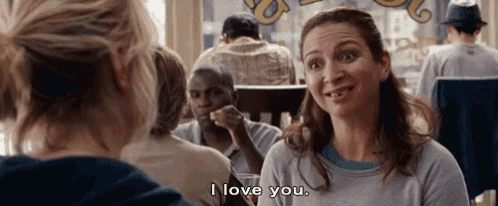 a woman is sitting at a table in a restaurant talking to another woman and saying i love you .