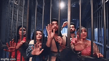 a group of people are standing in a jail cell with their hands up .