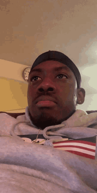 a man wearing a headband and a hoodie looks at the camera with a clock in the background