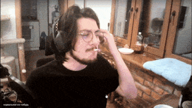 a man wearing glasses and headphones is smoking a cigarette in front of a window