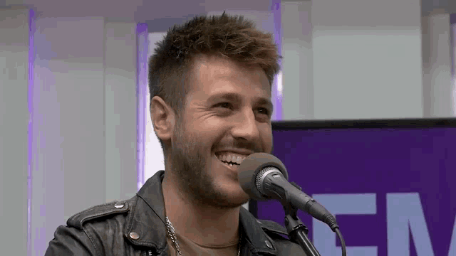 a man in a leather jacket is singing into a microphone and smiling