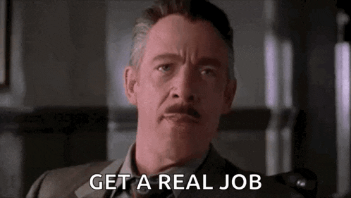 a man with a mustache is sitting in a chair with the words `` get a real job '' written on his face .