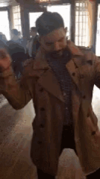 a man in a tan trench coat is dancing in a room