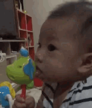 a baby in a striped shirt is holding a toy in his mouth .