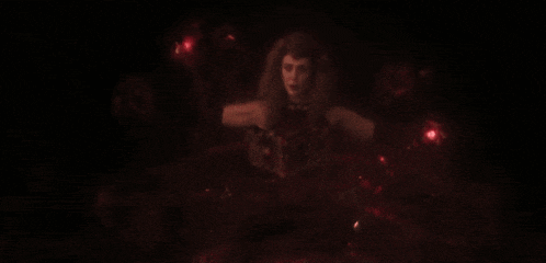 a woman with red eyes is standing in the dark holding a red object .