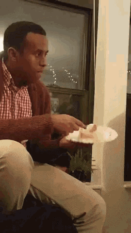 a man is sitting in front of a window and eating a piece of cake