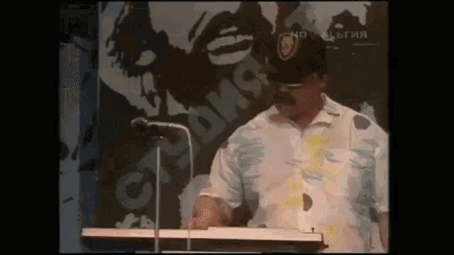 a man in a hat stands at a podium in front of a sign that says " socialism "