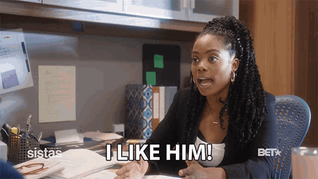 a woman is sitting at a desk and says " i like him "