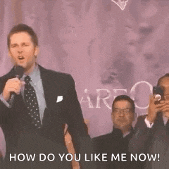 a man in a suit and tie is holding a microphone and talking to a crowd .