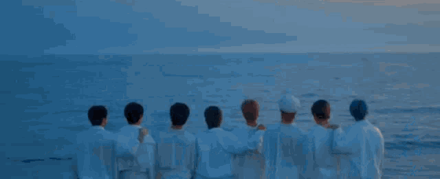 a group of young men in white shirts are walking on the beach holding hands .