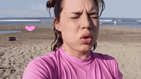 a woman wearing a pink shirt is taking a selfie on the beach