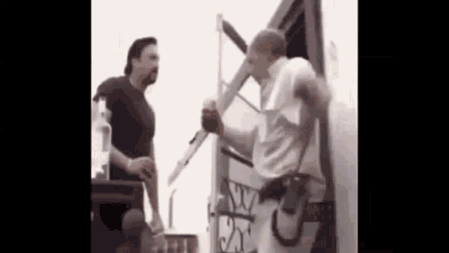 two men are standing next to each other in front of a door . one of the men is holding a knife .