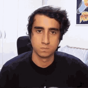 a young man with curly hair is sitting in a chair and making a face .