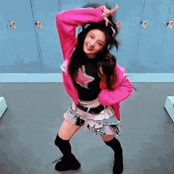 a woman is dancing in a locker room wearing a pink jacket and a black top .