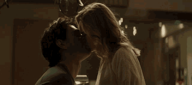 a man and a woman are kissing in a room with christmas lights in the background .