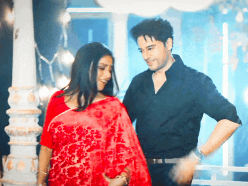 a man in a black shirt stands next to a woman in a red sari