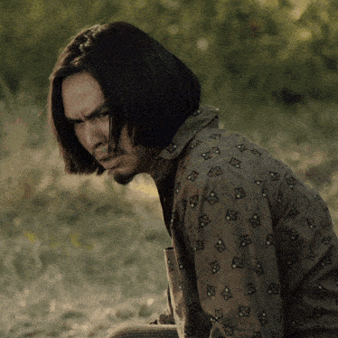 a man with long hair and a beard is wearing a brown shirt with a pattern of squares