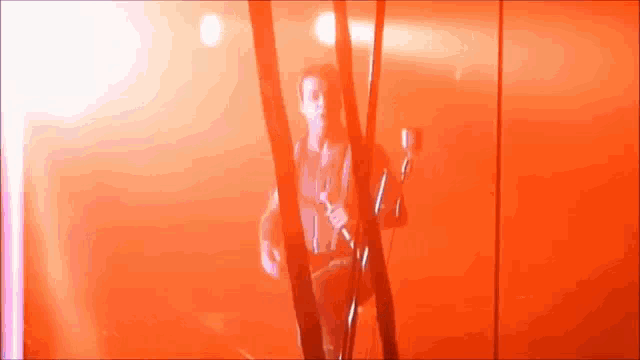 a man playing a guitar in front of a red wall