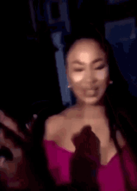 a woman in a pink off the shoulder top is waving her hand in the dark .