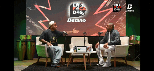 two men are sitting in front of a betano banner