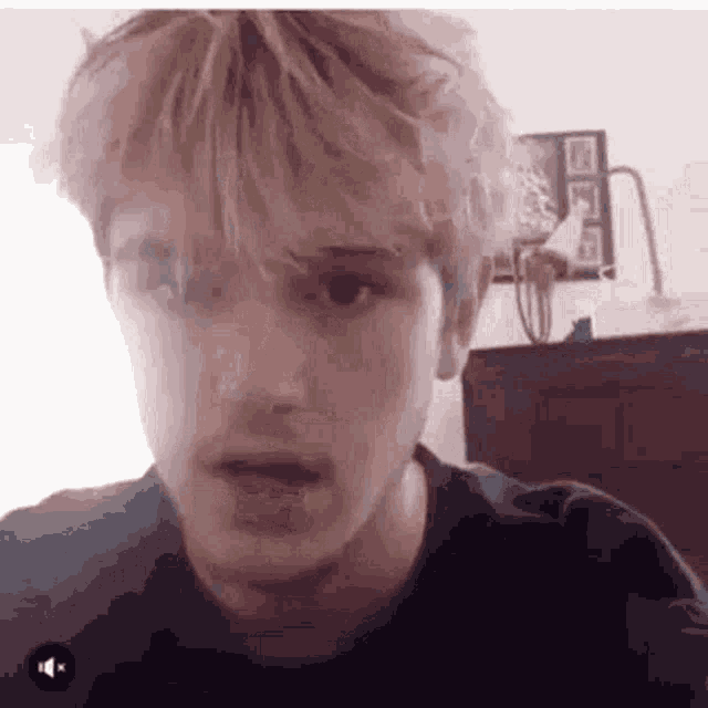 a young man with blonde hair is looking at the camera while sitting in front of a table .