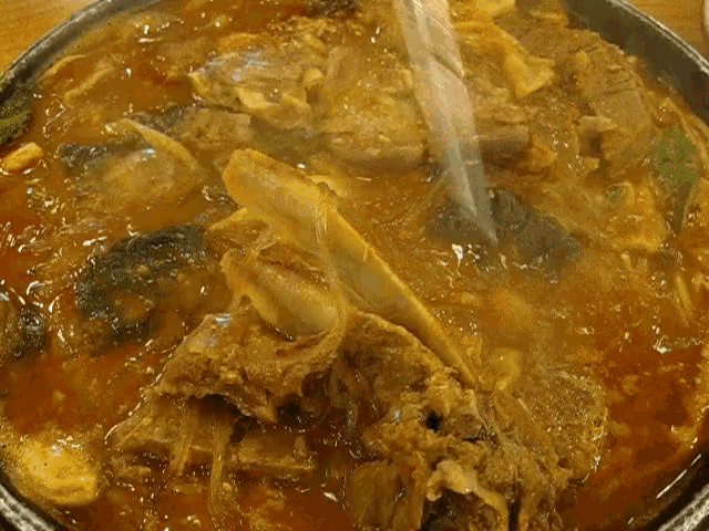 a person is taking a piece of meat out of a pot of soup with chopsticks .