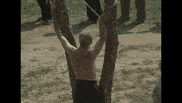 a man is tied to a tree with ropes while another man watches .