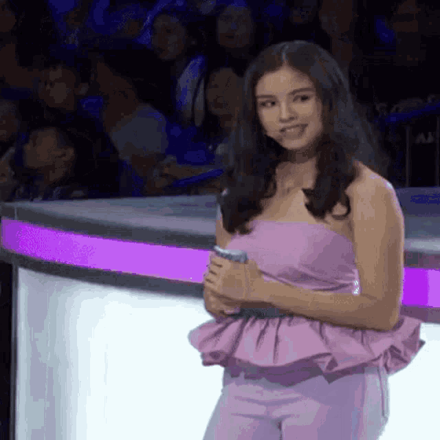 a woman in a purple dress is standing in front of a crowd and holding a cell phone .