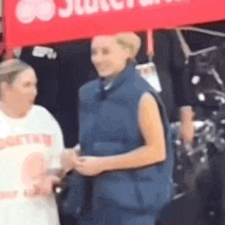 a woman in a blue vest is standing next to a woman in a white shirt .
