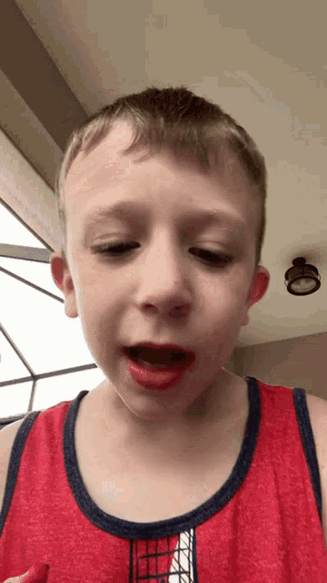 a young boy wearing a red tank top with a spiderman logo