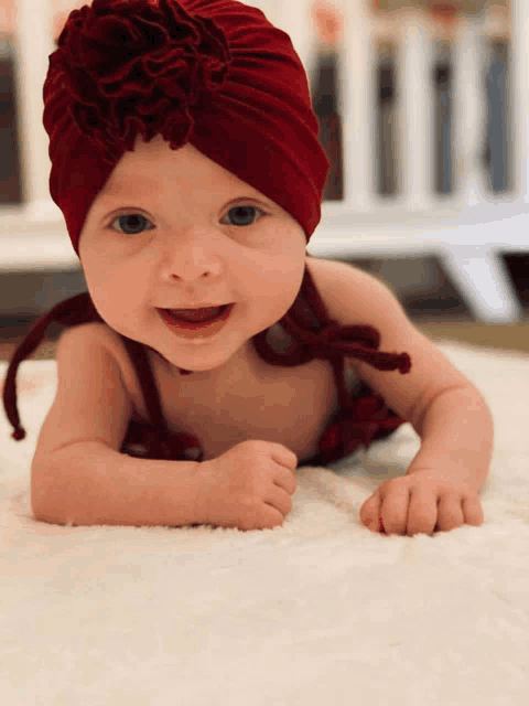 a baby wearing a red turban is laying on its stomach and smiling