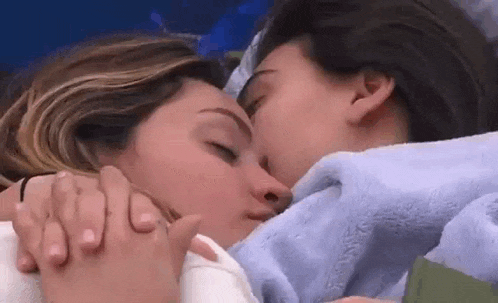 two women are kissing each other while laying under a blanket in bed .