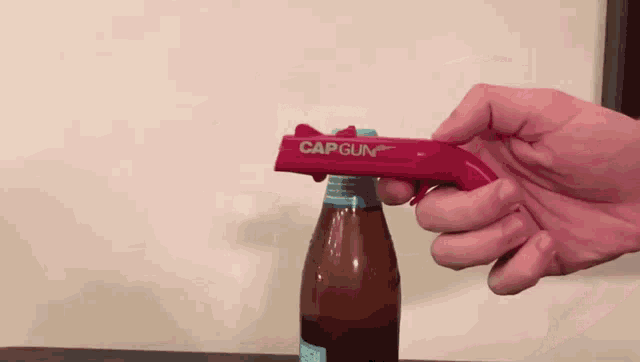 a person is opening a bottle with a red cap gun
