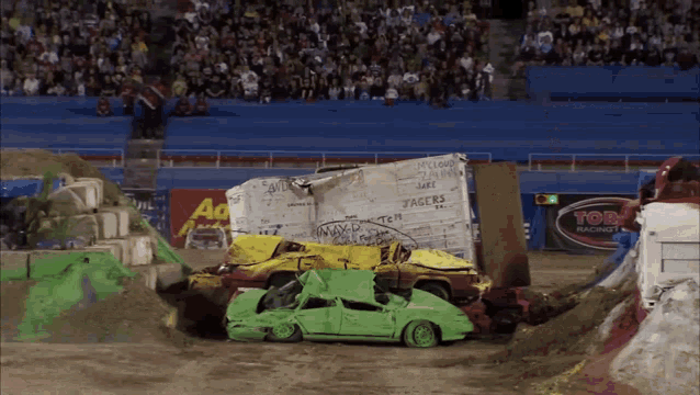 a green car crashes into a yellow car in front of a top racing sign
