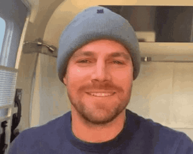 a man with a beard wearing a blue beanie and a blue shirt is smiling .