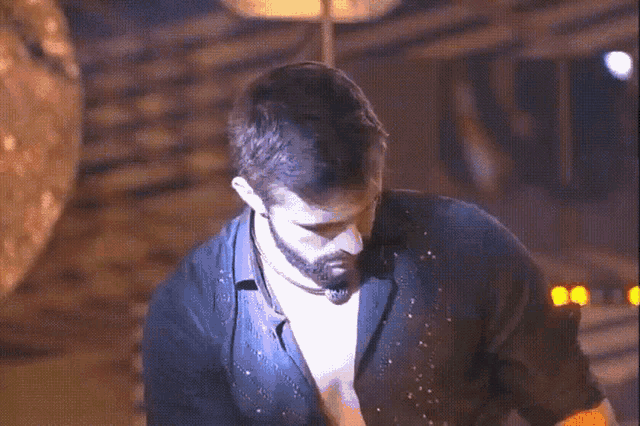 a man with a beard and a black shirt is standing in a dark room with a blue light behind him .