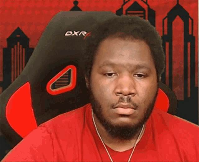 a man wearing a red shirt is sitting in a red and black dxr4 chair