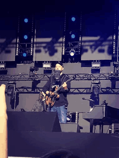 a man singing into a microphone while playing a guitar on stage