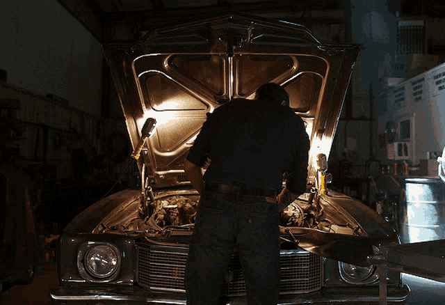 a man with a tattoo on his arm stands in front of a car with its hood up