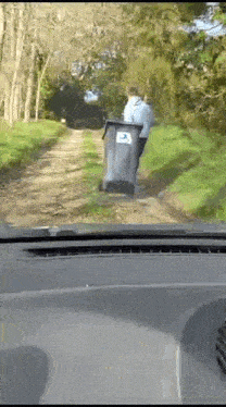 a man pushing a trash can down a dirt road
