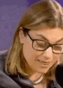 a close up of a woman wearing glasses and a necklace talking into a microphone .