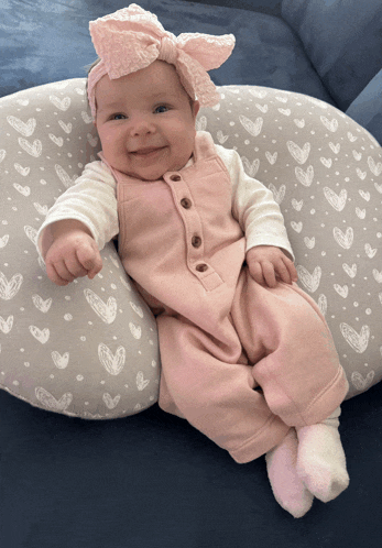 a baby wearing a pink outfit and a headband is sitting on a pillow with hearts on it