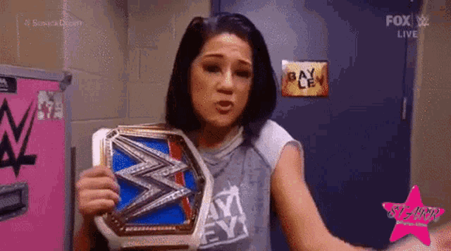 a woman is holding a wrestling championship belt in front of a sign that says bayley .