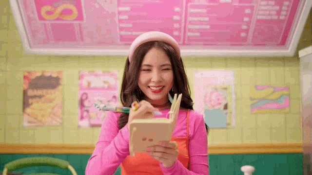 a girl in a pink shirt is writing in a notebook and smiling