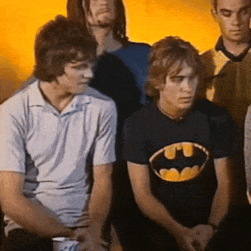 a man wearing a batman t-shirt sits in a group of young men