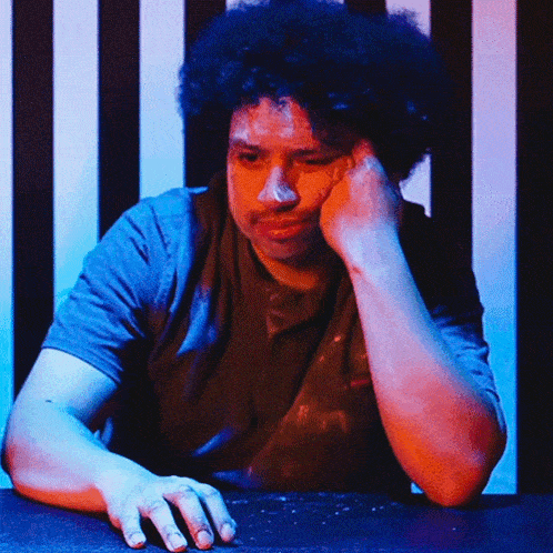 a man with curly hair is sitting at a table with his hand on his face
