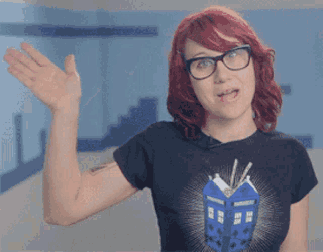 a woman with red hair wearing glasses and a black shirt with a blue box on it