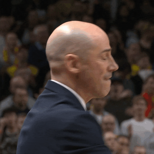 a bald man in a suit and tie stands in front of a crowd of people