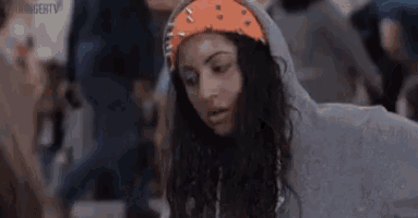 a woman wearing a hoodie and an orange headband is standing in front of a crowd .