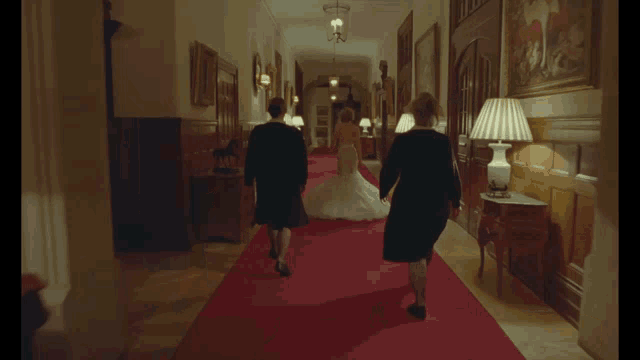 a woman in a wedding dress is walking down a hallway with two women